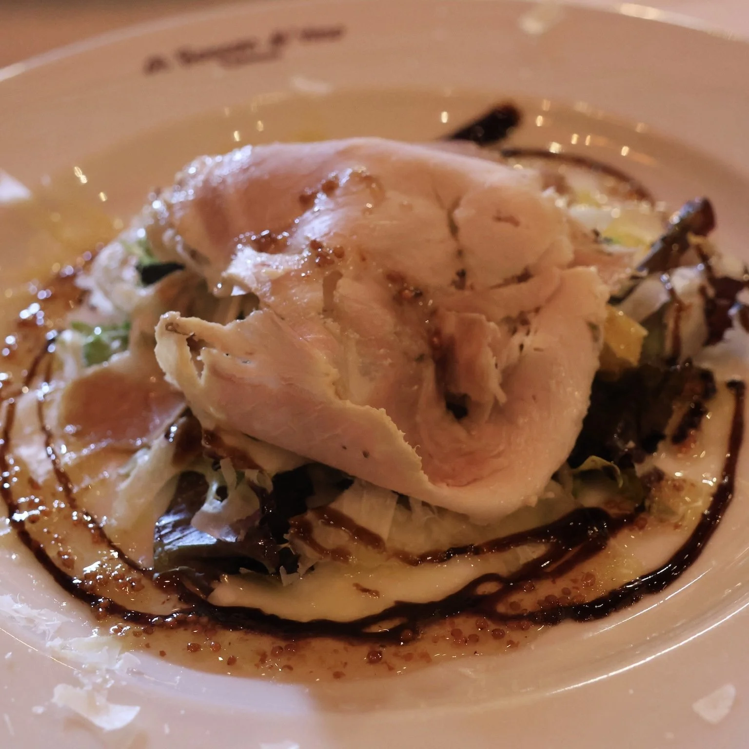 Close-up of a plate with slices of grilled chicken, drizzled with dark sauce, and garnished with vegetables.