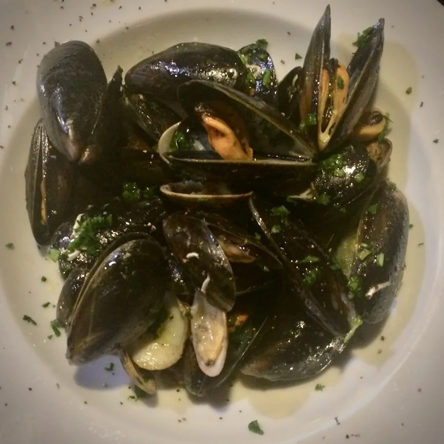 A white bowl filled with steamed mussels garnished with chopped parsley.