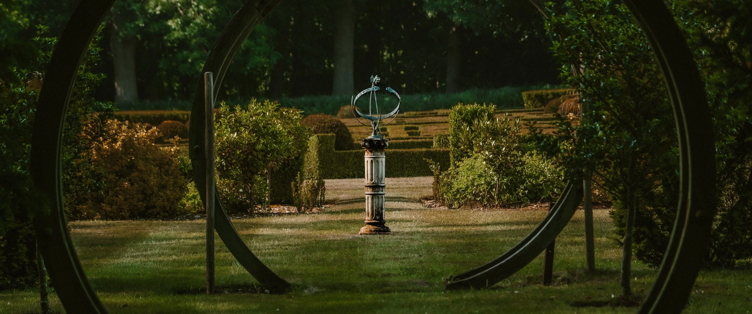 A garden sculpture of a Mercury statue on a pedestal, framed by circular metal structures.