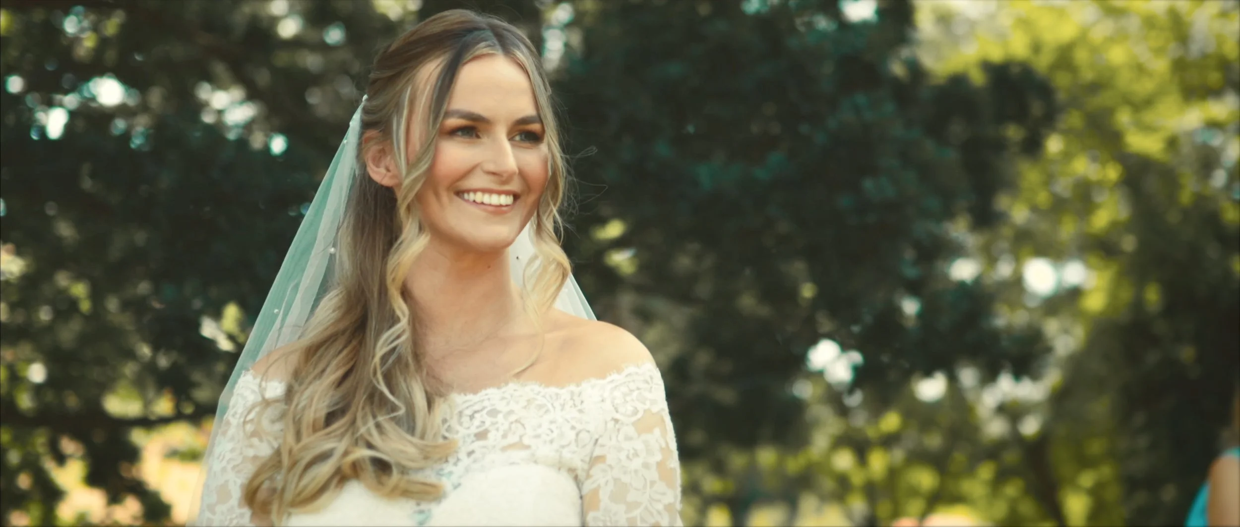 Bride smiling during an outdoor wedding portrait surrounded by natural light.