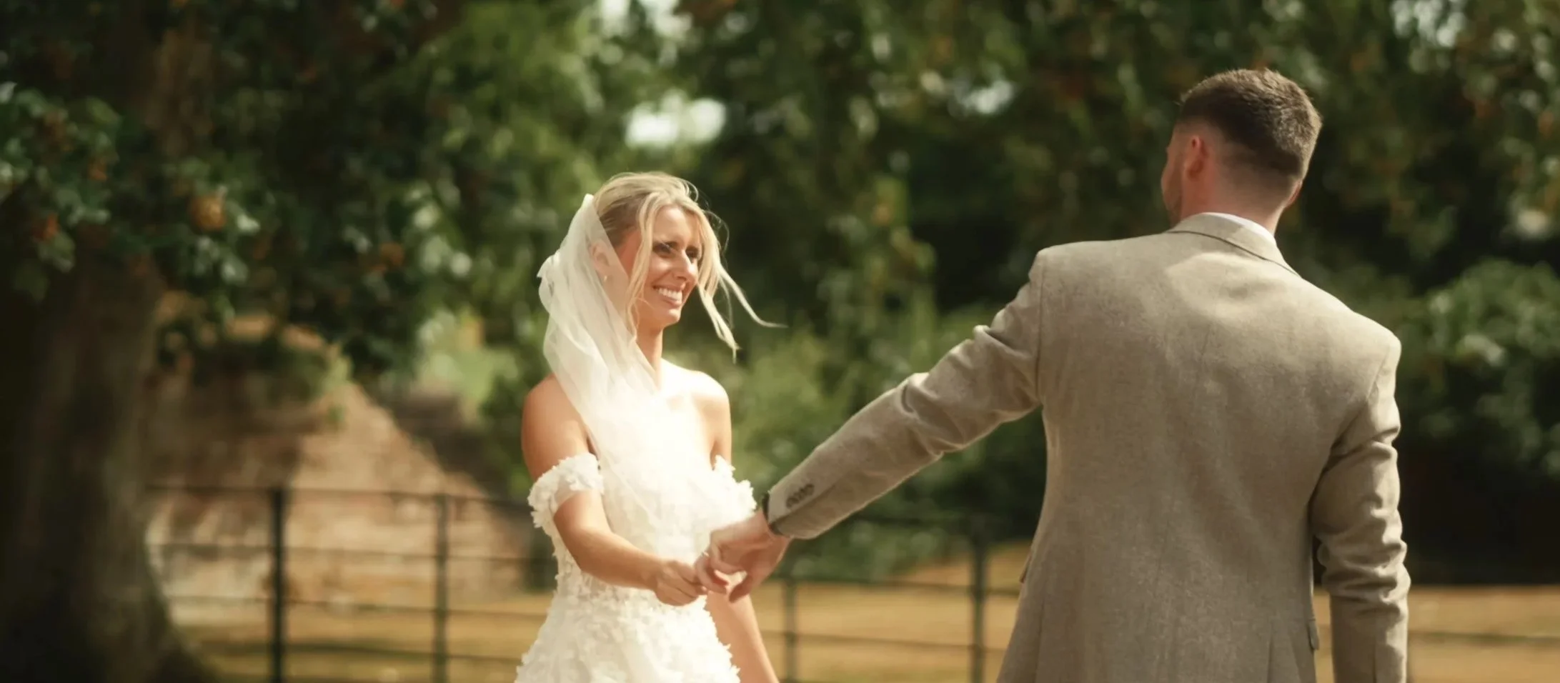 Bride and groom walking hand in hand through the gardens of a Suffolk estate during their wedding day, featured in a cinematic documentary wedding film.