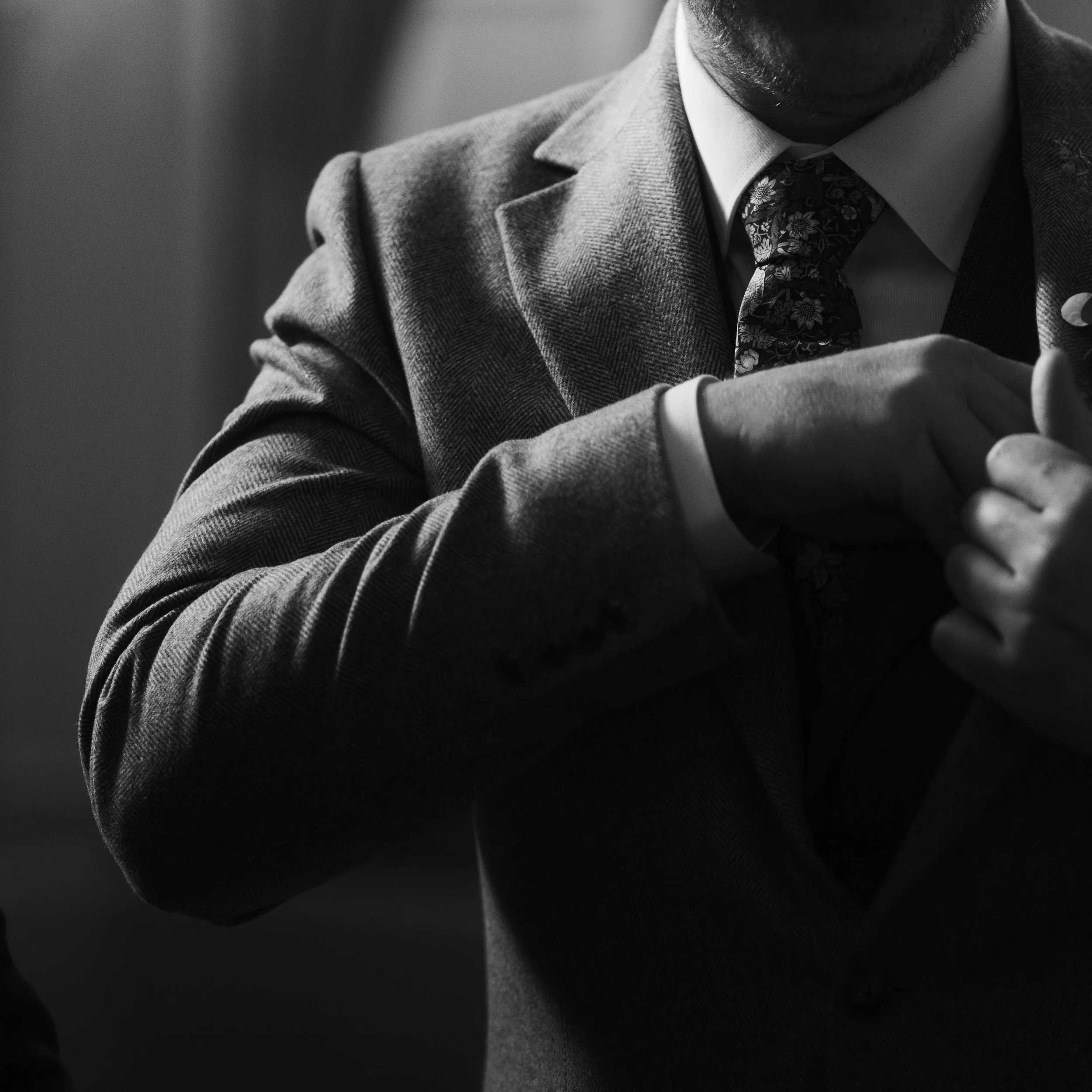 Black and white close-up of a groom adjusting his tie before the wedding ceremony.