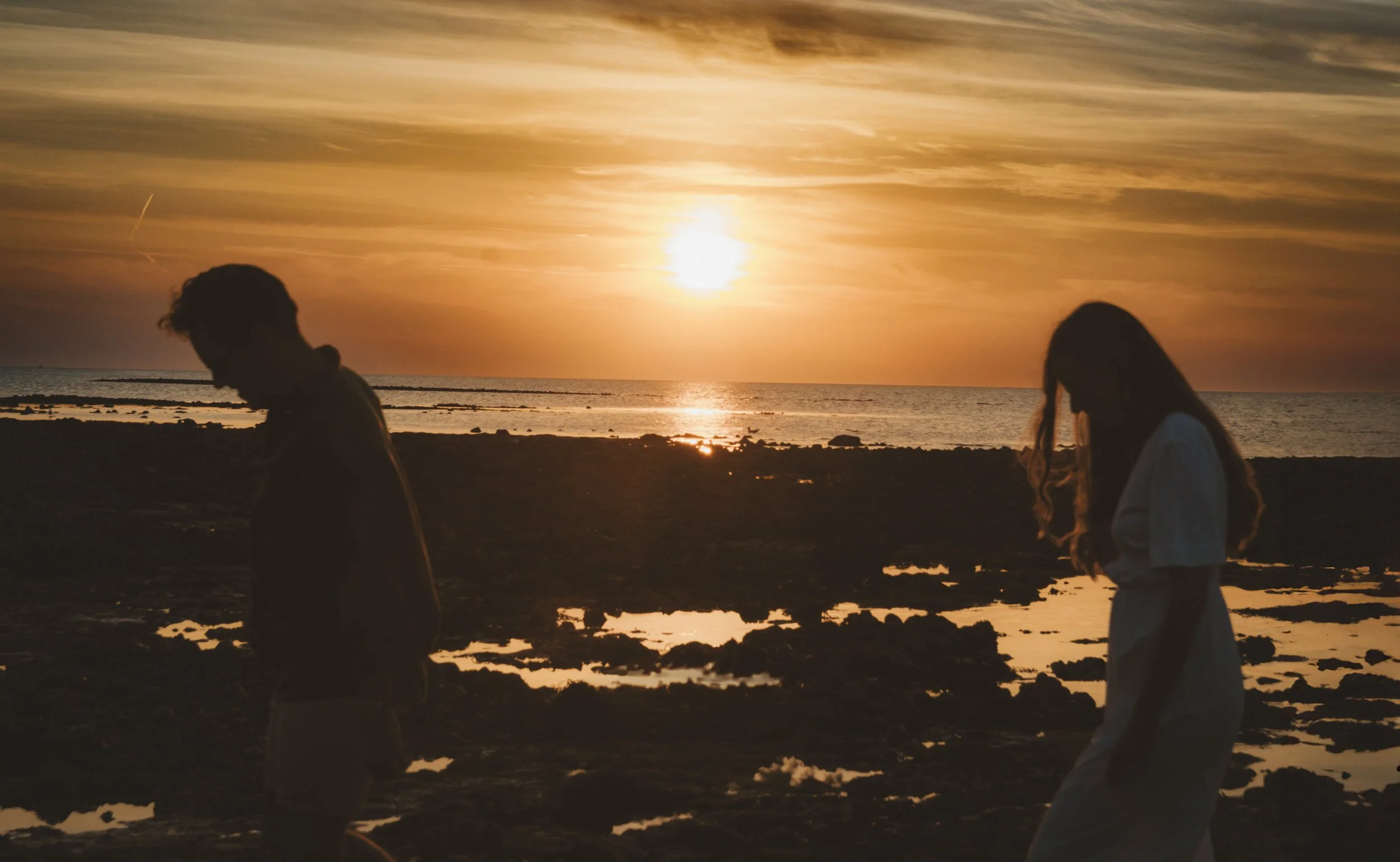Couple walking hand in hand along the Norfolk coast at sunset during their engagement shoot