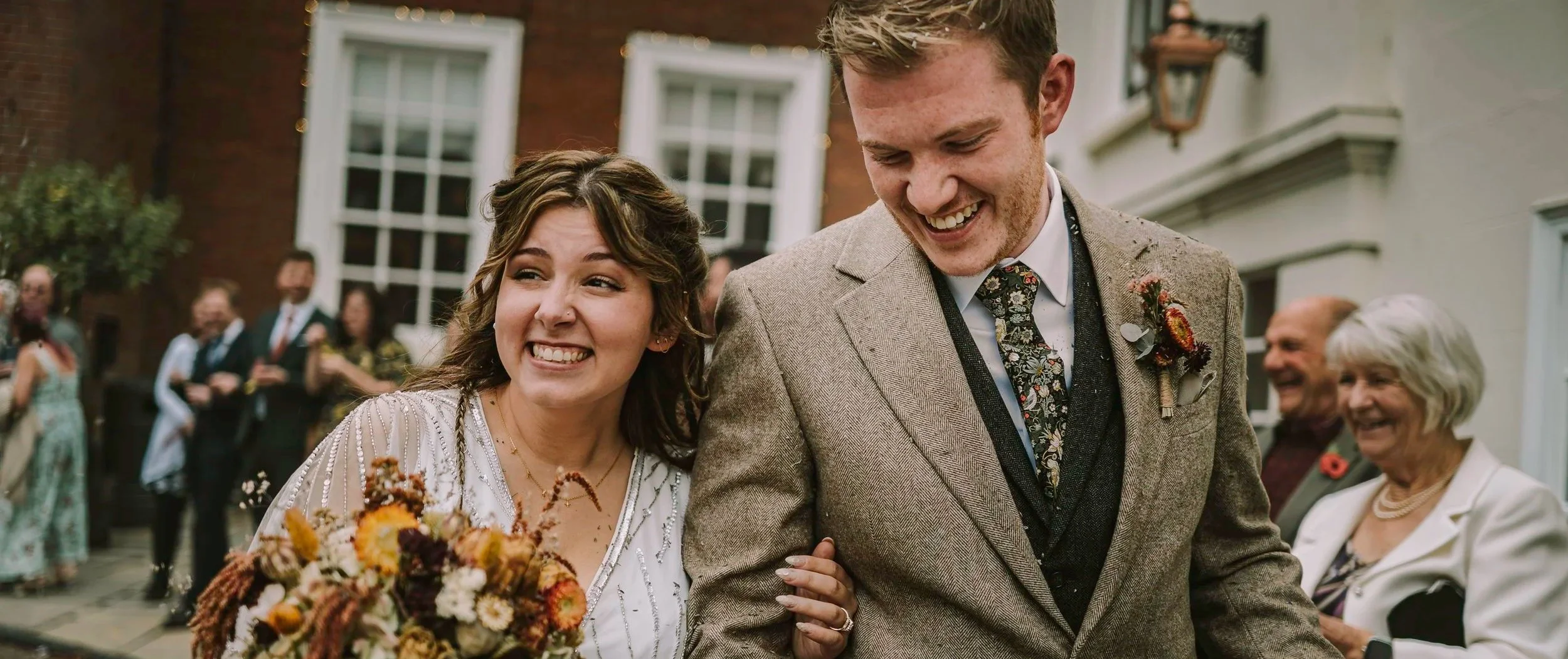 Bride and groom walking together after their wedding ceremony, smiling as guests celebrate around them.