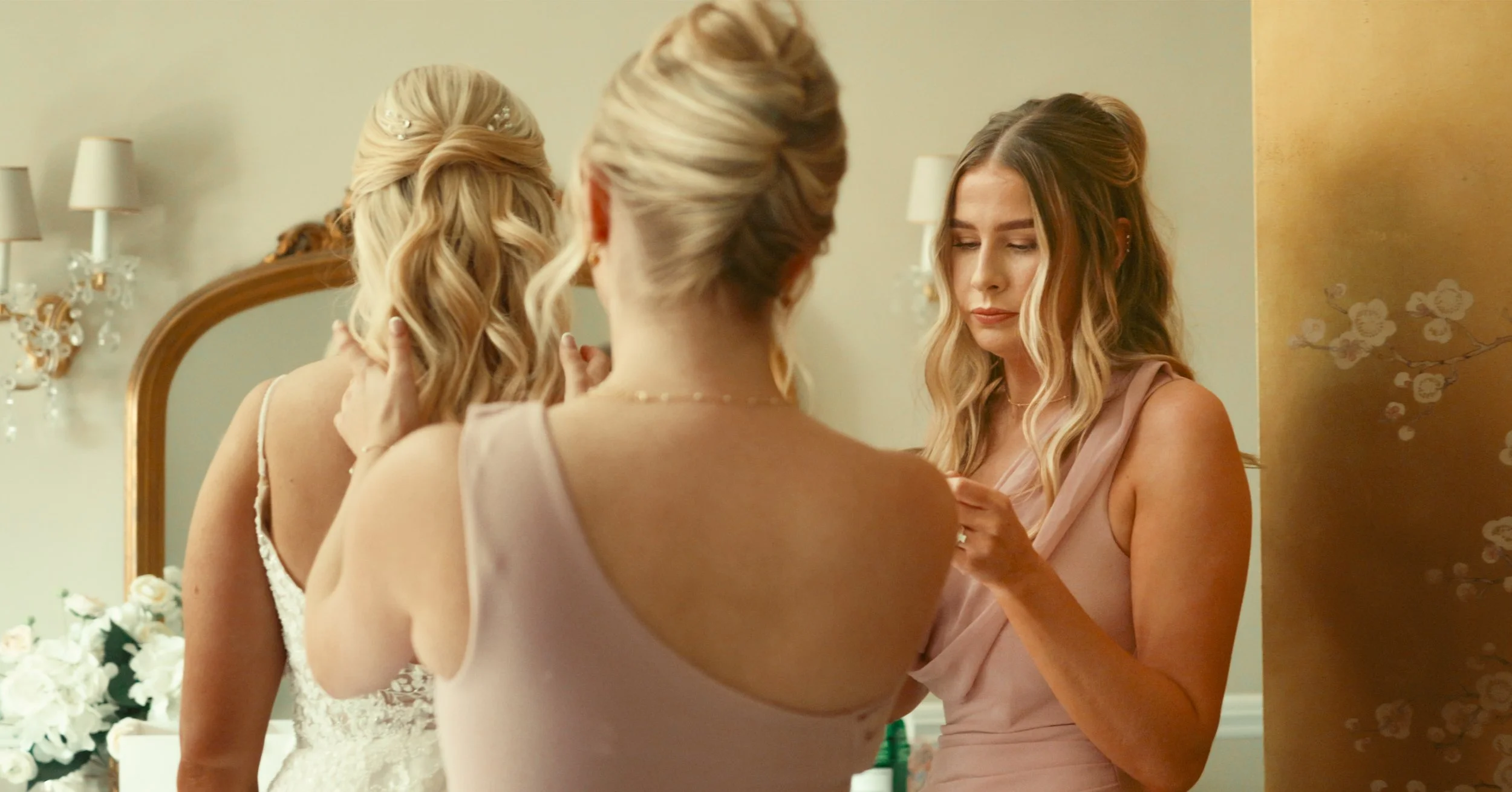 Bridesmaid fastening the bride's wedding dress during morning preparations.
