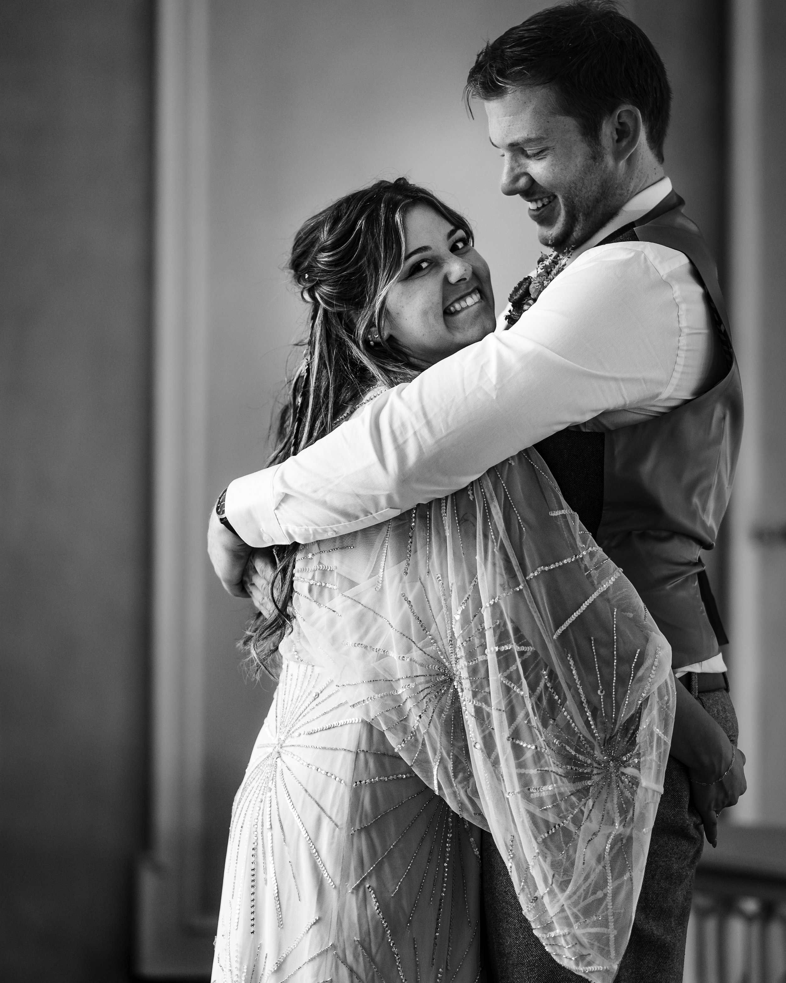 Bride and groom sharing a joyful embrace during their wedding reception in black and white.