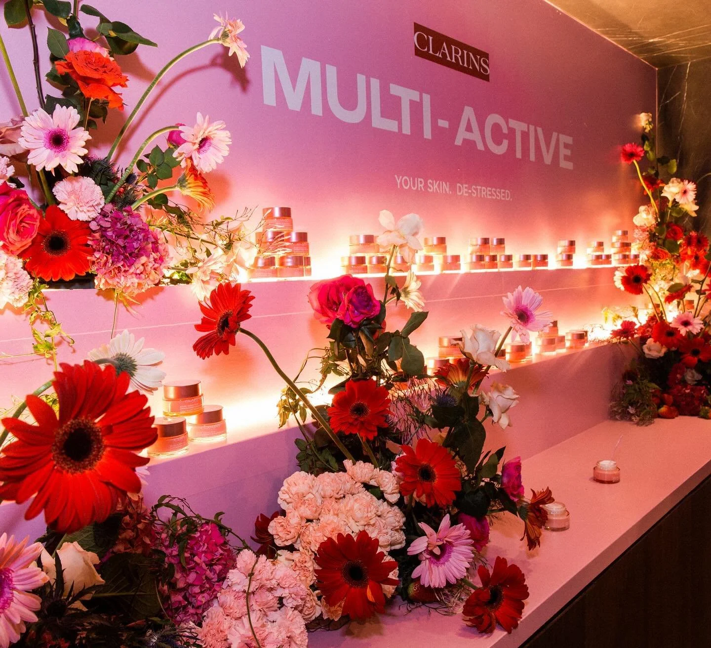 Display of skincare products on pink shelves decorated with colorful flowers, with signage reading 'CLARINS MULTI-ACTIVE' and the phrase 'Your skin, de-stressed'.