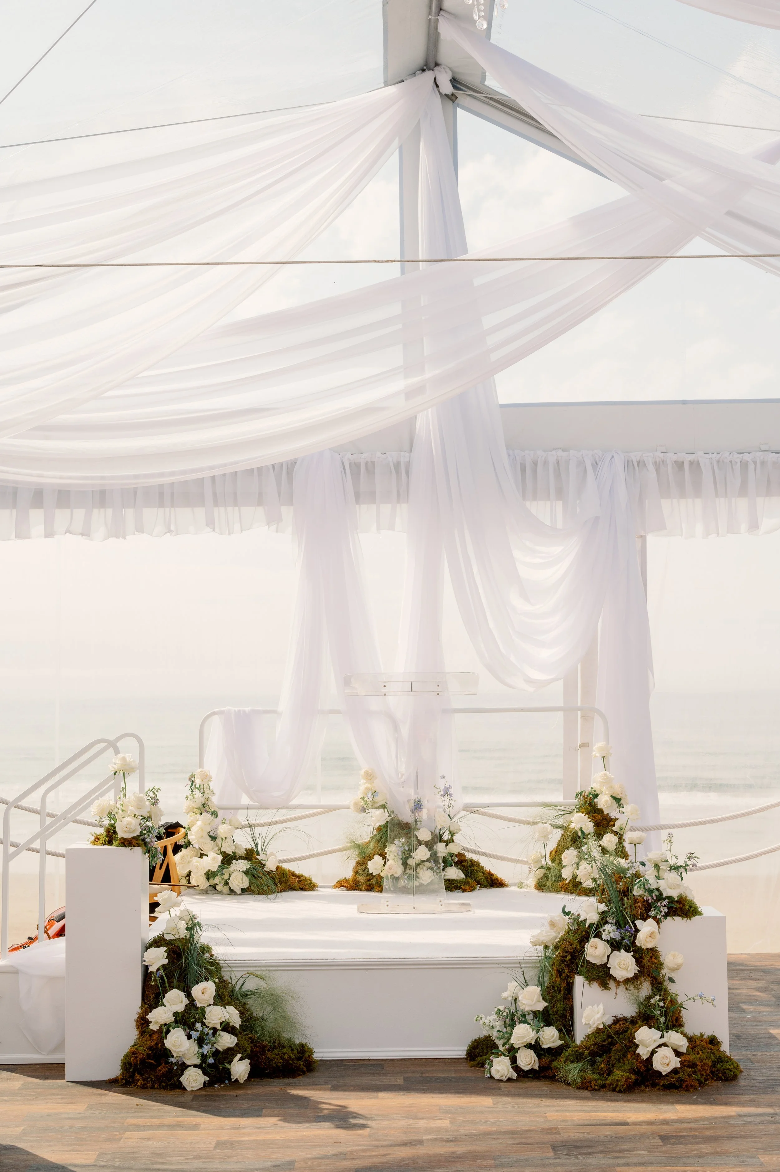 Wedding altar decorated with white drapery and flowers, set on a seaside location with ocean view