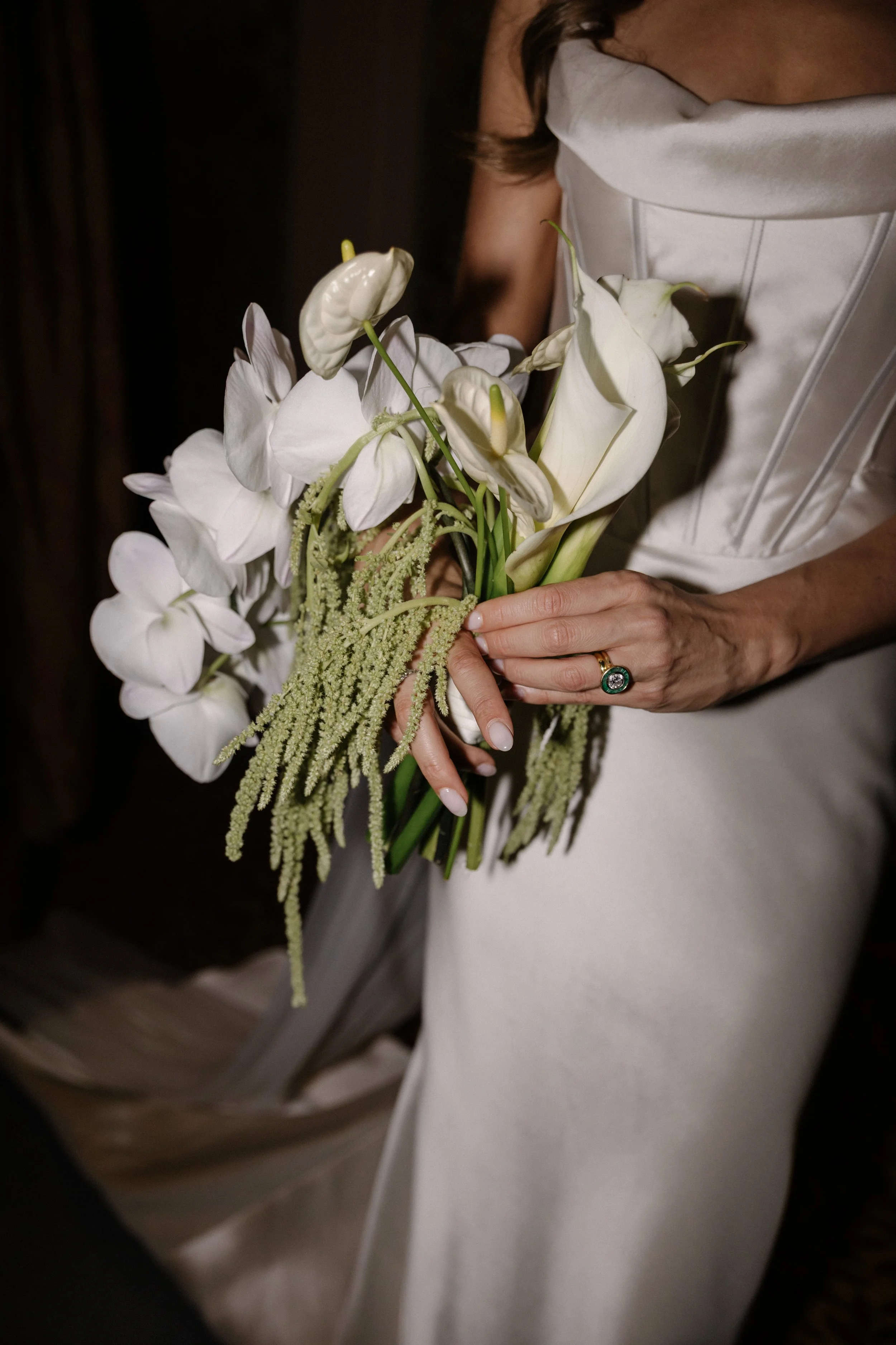 Close-up of a woman in a white dress holding a bouquet of white flowers, including calla lilies and orchids.