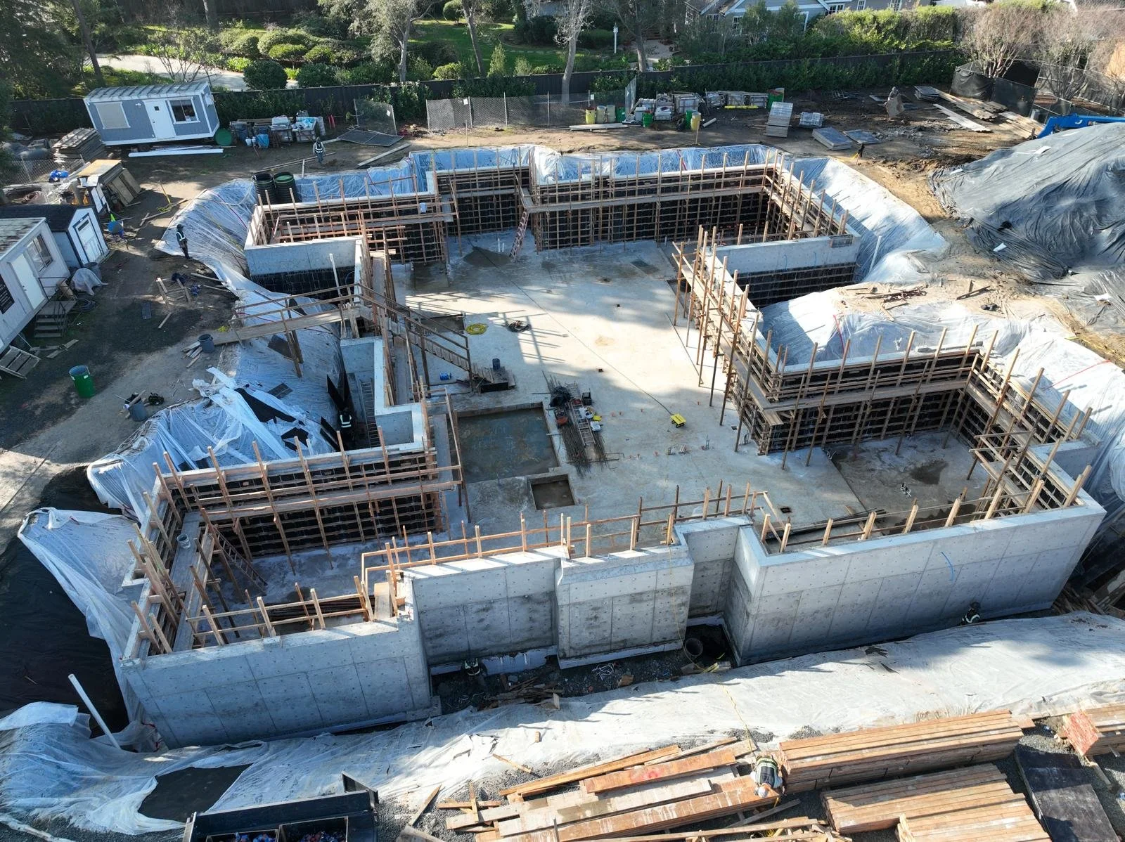 Aerial view of a construction site showing the early stages of building a house, with concrete foundation and wooden framing.