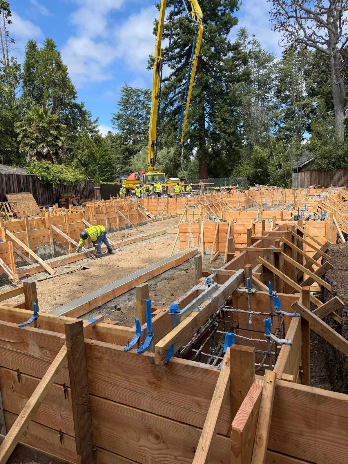 Construction workers building the foundation for a new house or building with wooden forms and a concrete pump truck.