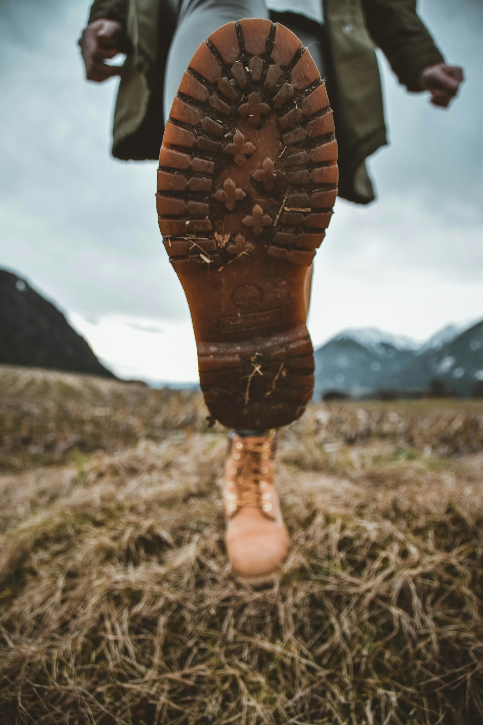 Close-up of a person's boot sole, with a natural outdoor background and mountains in the distance.