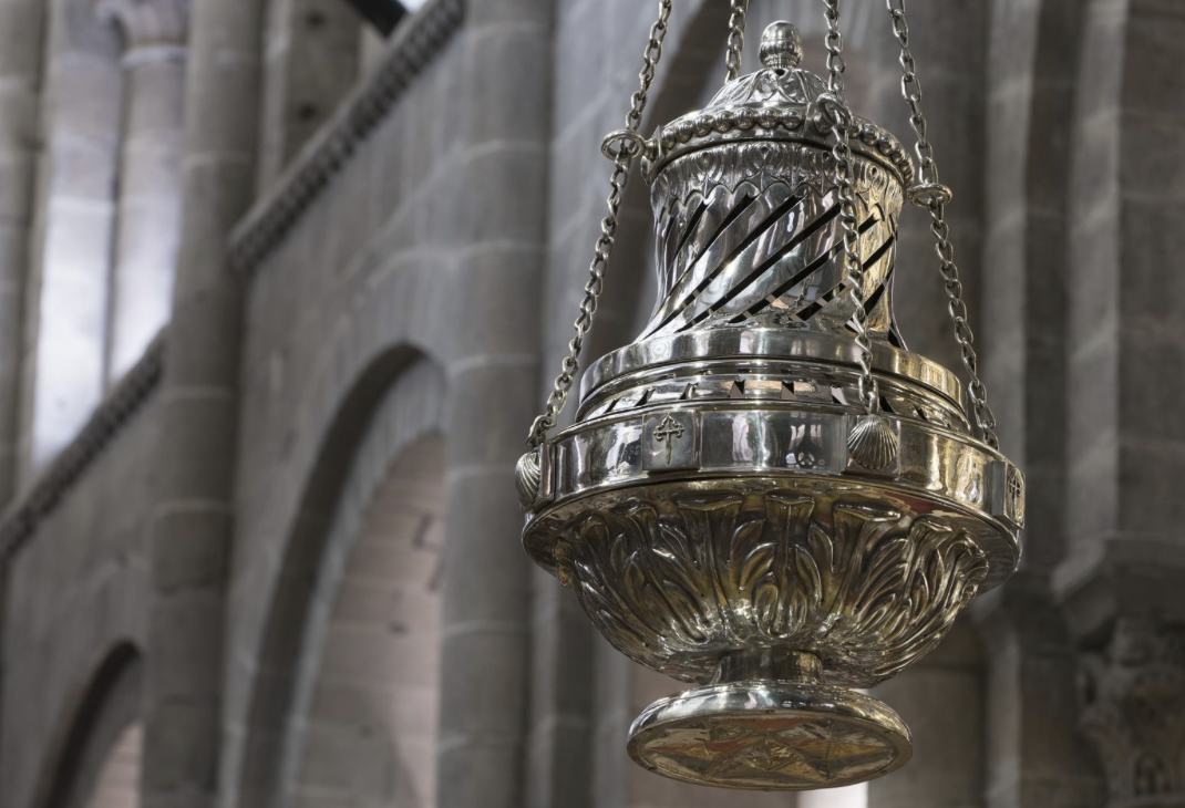 Close-up of the silver-plated Botafumeiro censer hanging by chains inside Santiago Cathedral, with stone arches in the background.
