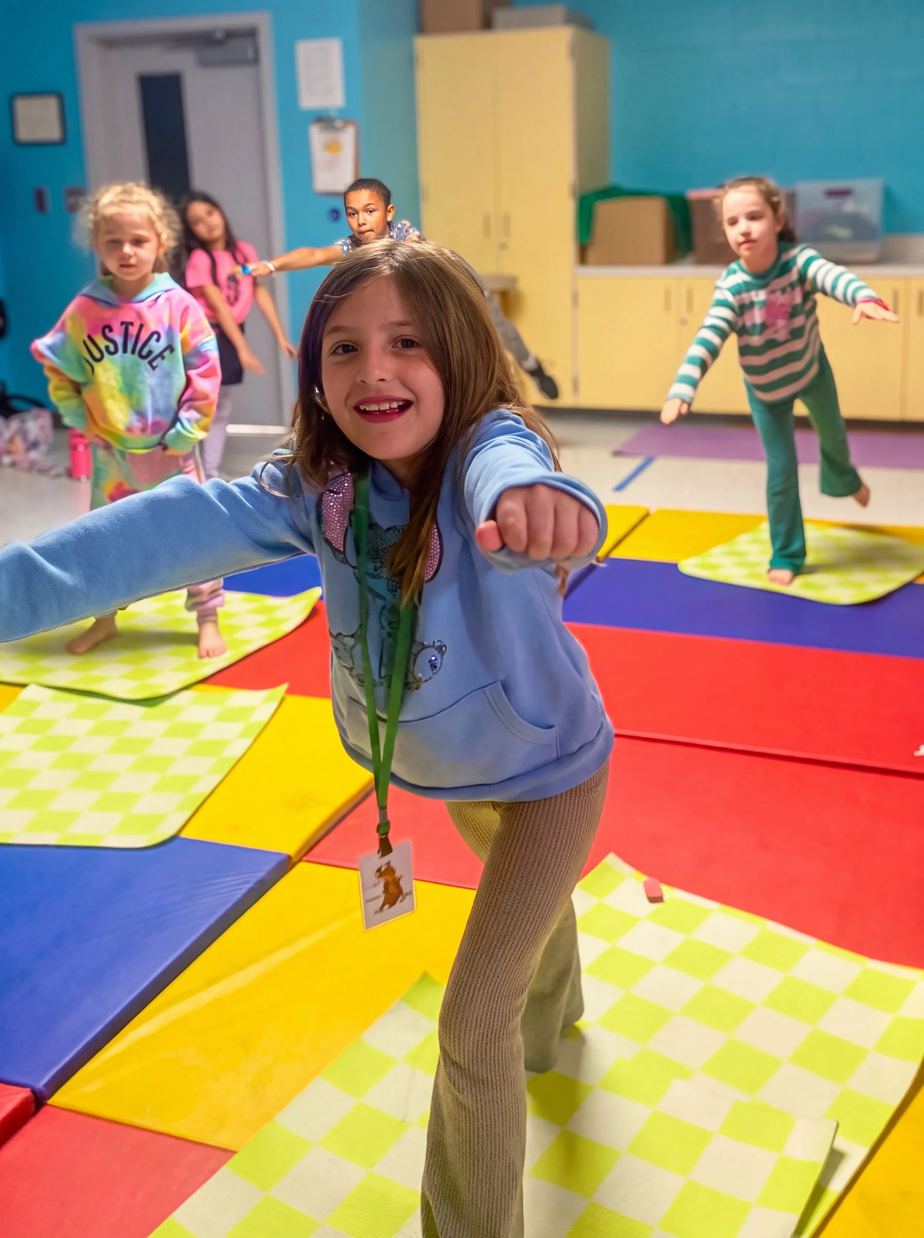 Children practicing yoga or stretching on colorful mats in a classroom or gym setting.
