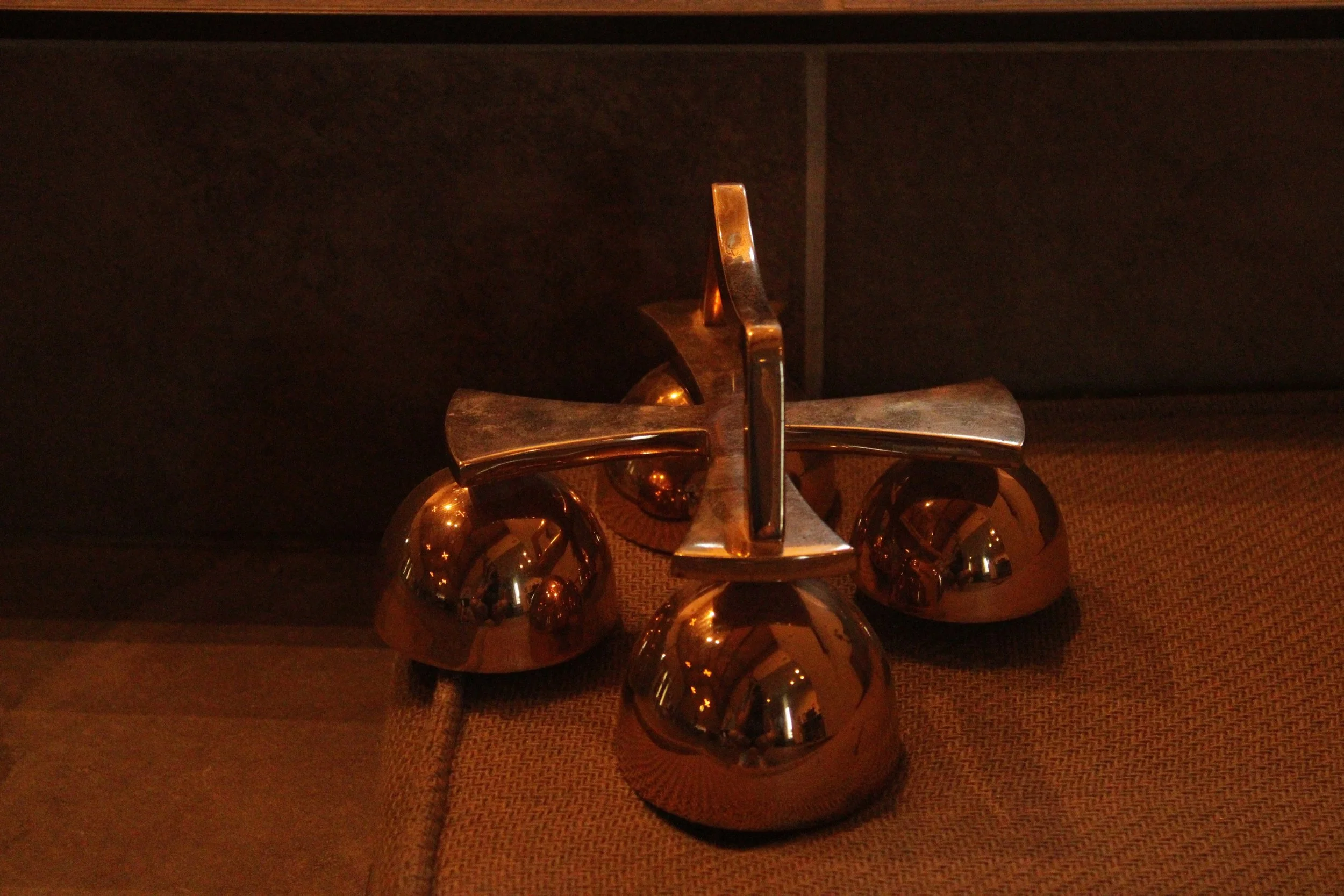 A small metallic car sculpture with a shiny, reflective surface, positioned on a textured fabric surface against a dark background.