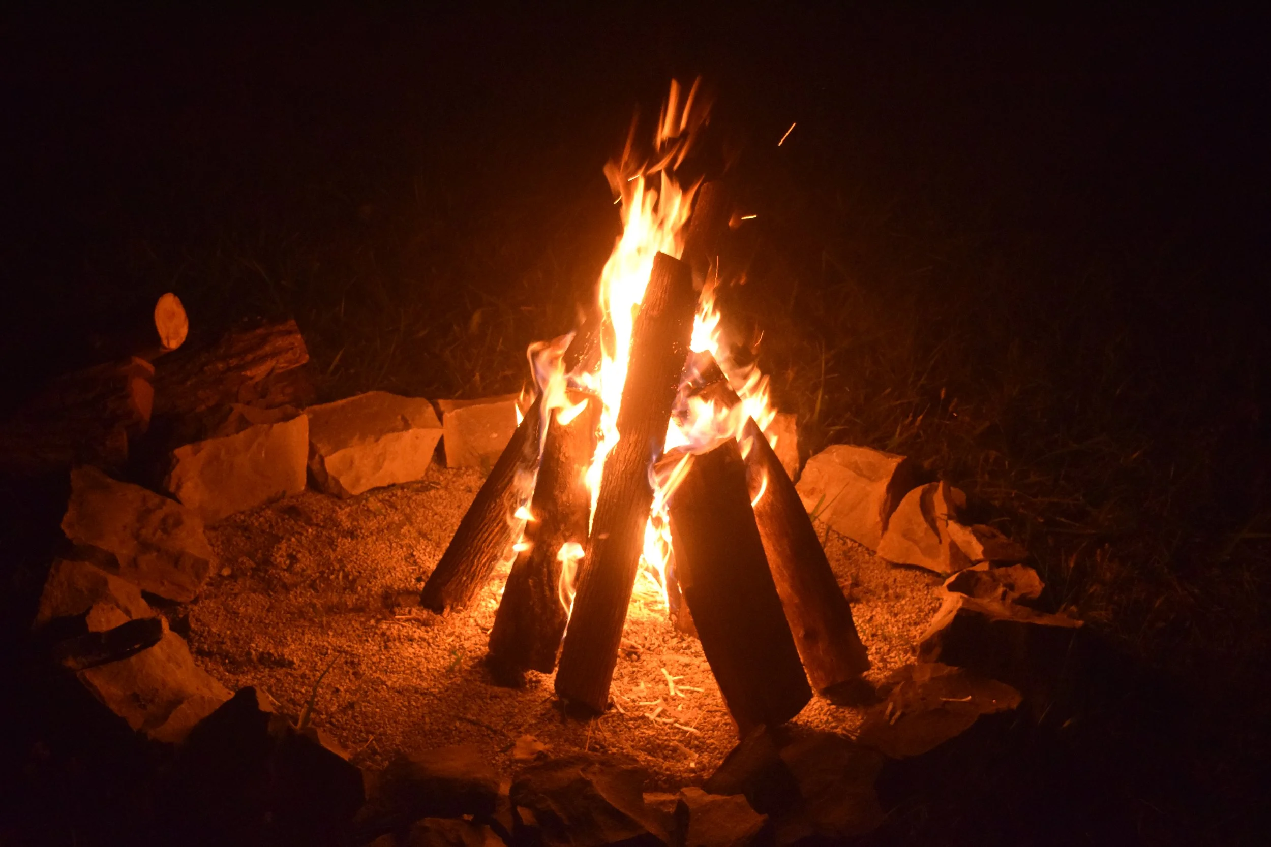A campfire burning with logs surrounded by rocks at night.