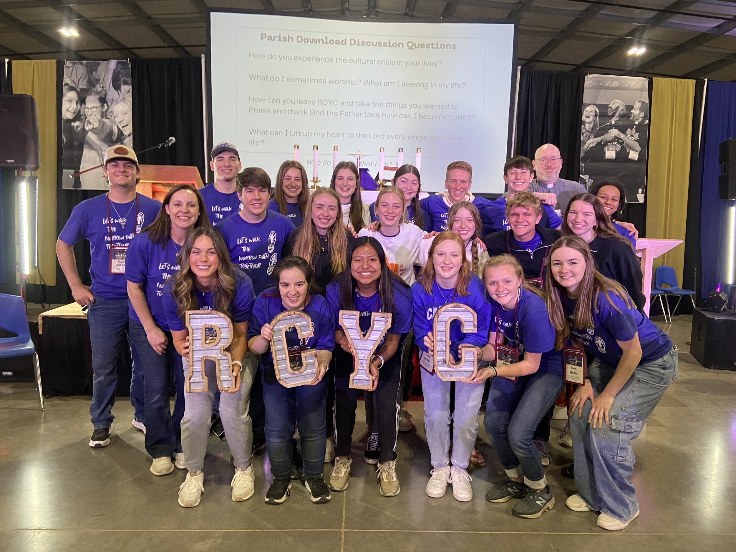 Group of young people and an adult man wearing purple shirts and holding large wooden letters forming 