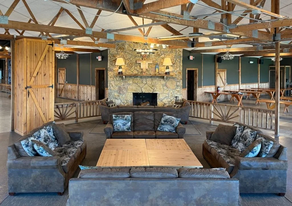 Indoor lounge area with a stone fireplace, wooden beams, and rustic decor, including several sofas and tables.