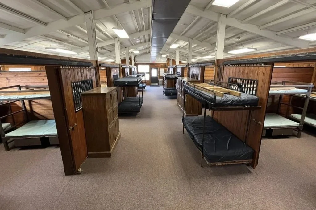 Dormitory with wooden cubicles and metal bunk beds in a large, open space