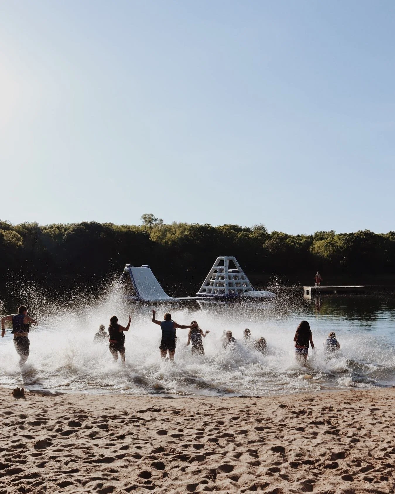 Children and adults playing in the water at a beach with a large waterslide in the background.
