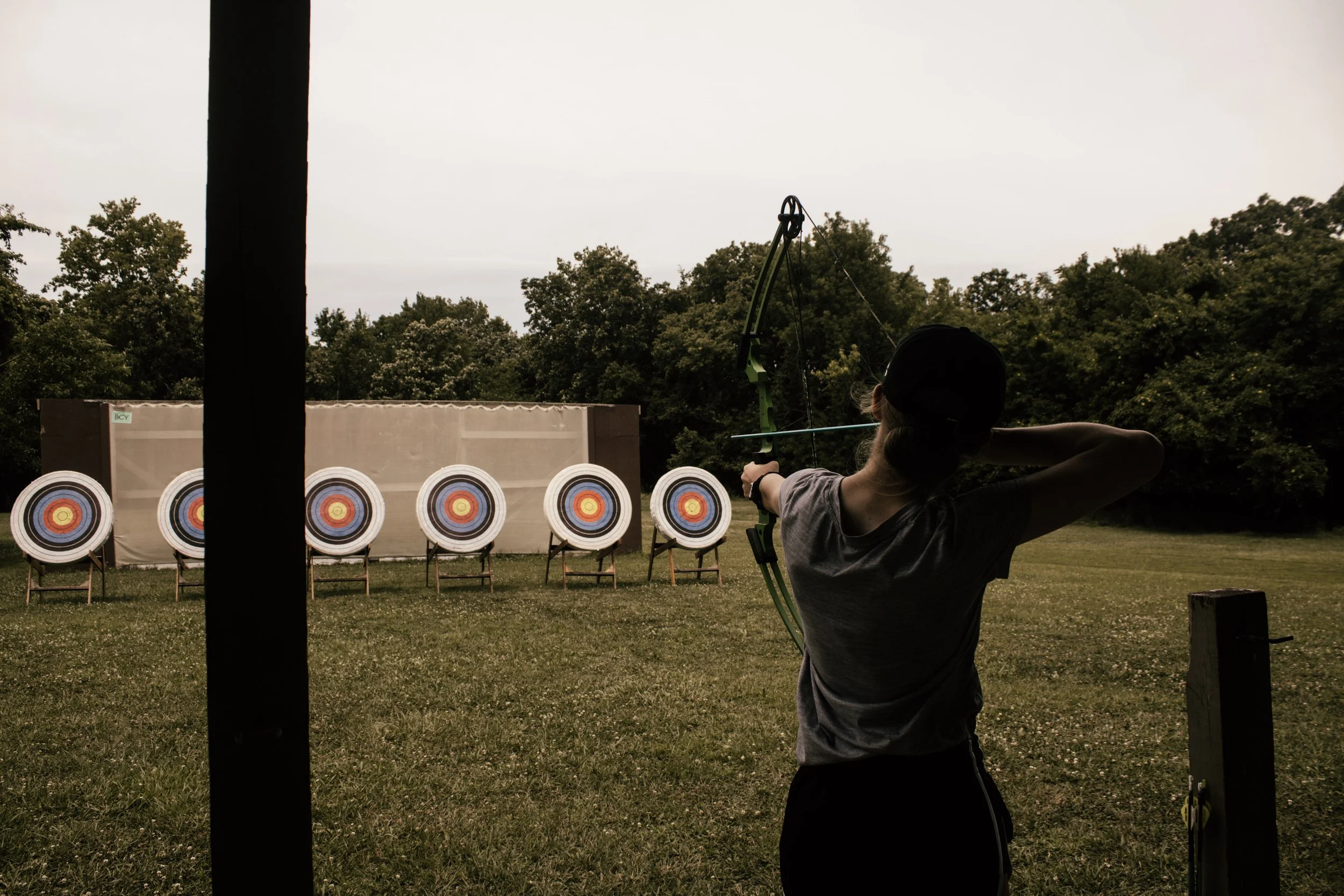 Person practicing archery outdoors aiming at a row of target targets.