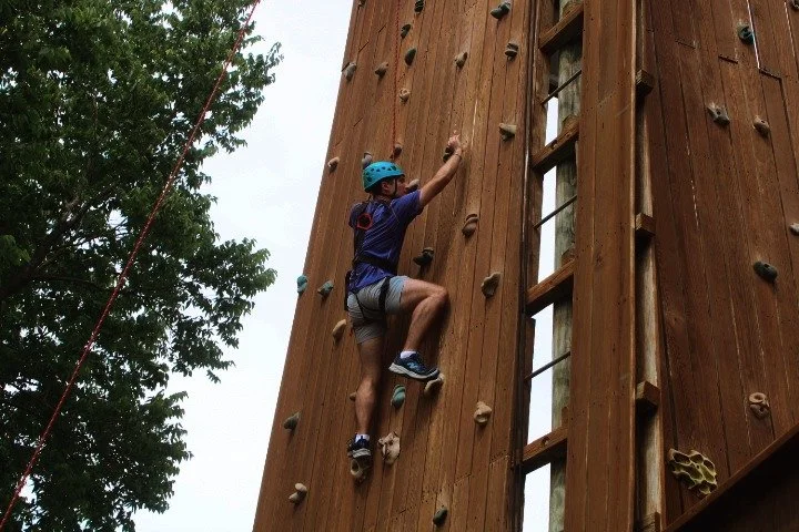 Person wearing a blue helmet climbing an outdoor wooden rock climbing wall.