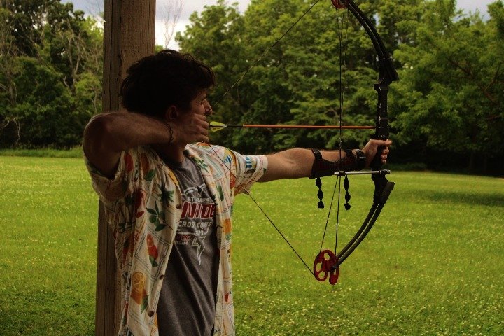 Person practicing archery outdoors, aiming a bow and arrow.