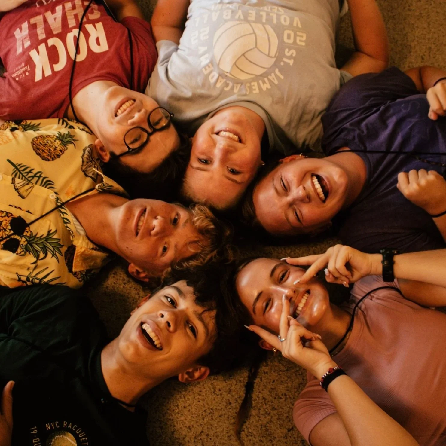Group of diverse young adults lying on the floor in a circle, smiling and taking a selfie.