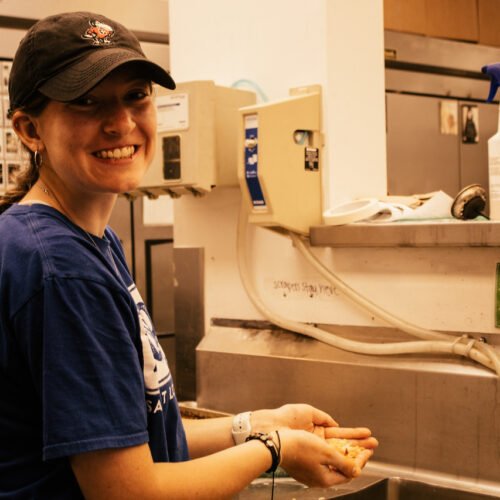 A young woman smiling while washing her hands in a kitchen.