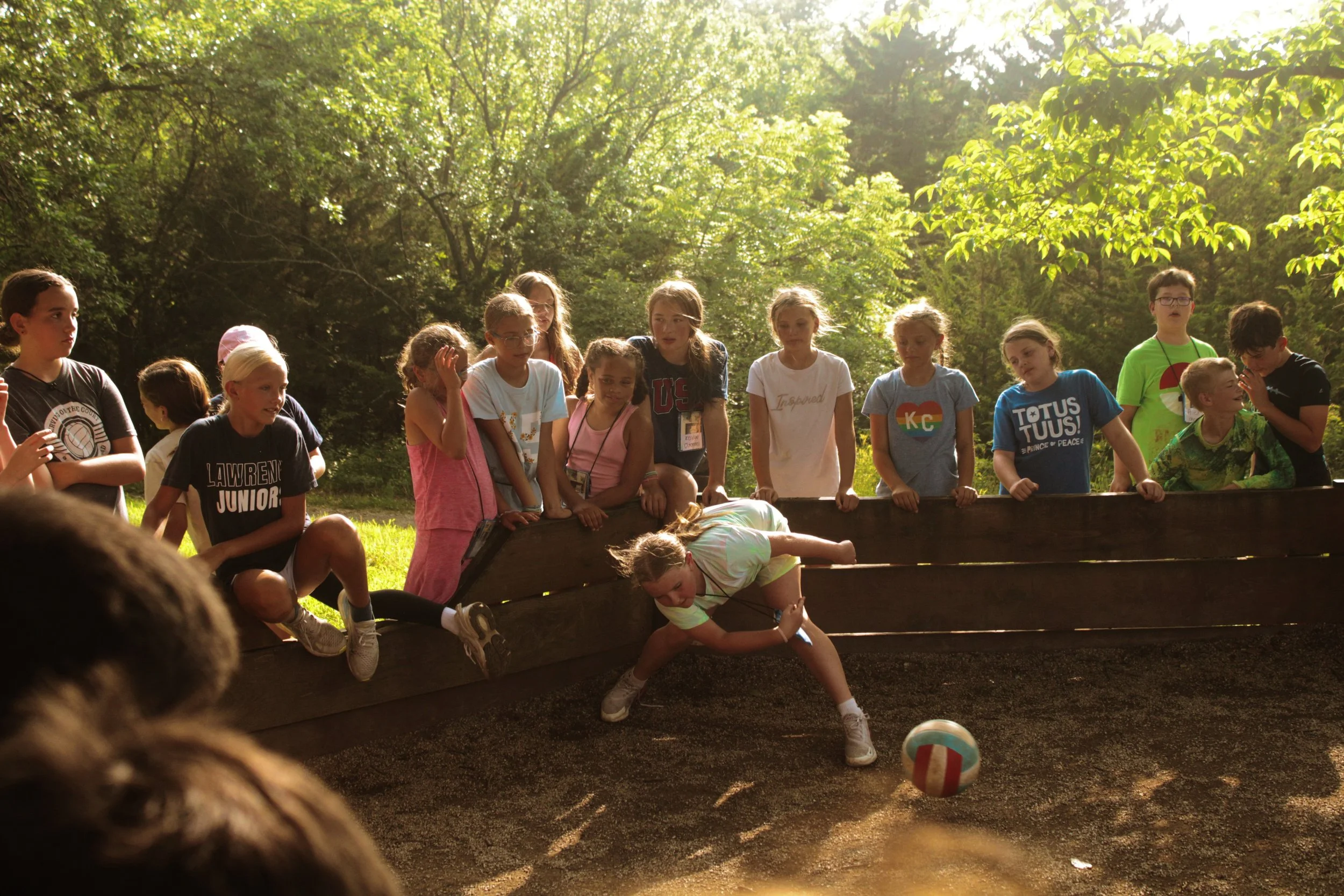 Group of children playing a game outdoors in a wooded area on a sunny day.