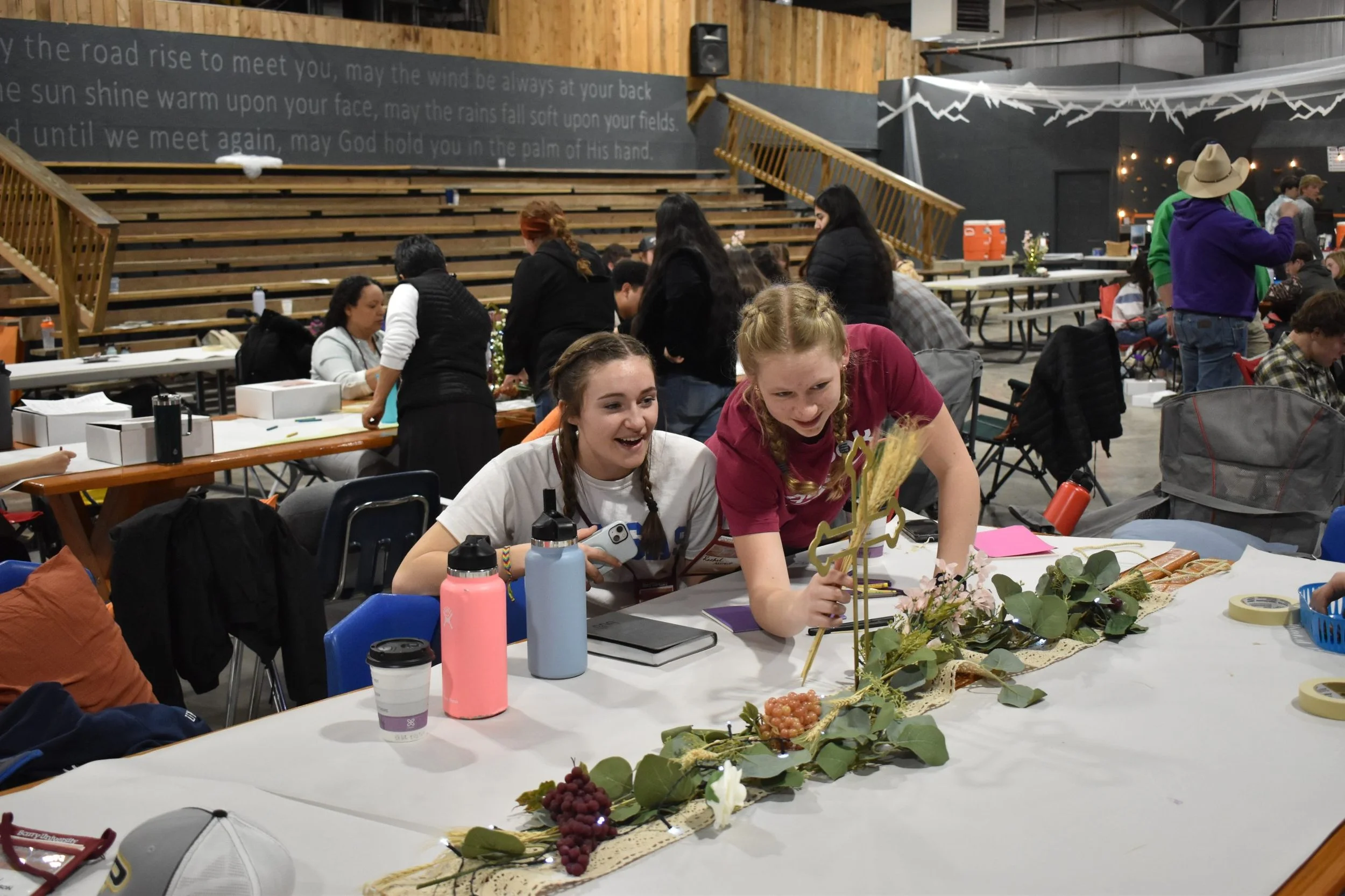 People gathered around tables at an indoor event, with decorations, flowers, and drinks visible on the tables.