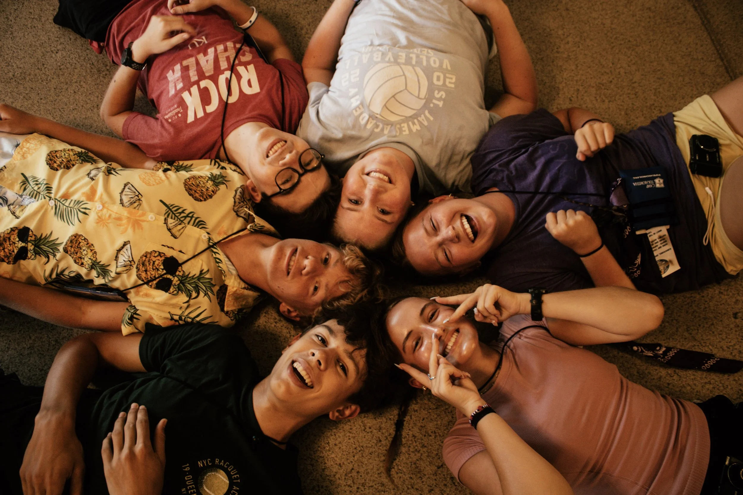 Group of people lying on carpeted floor, smiling and making peace signs.