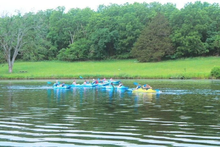 People kayaking on a river with green trees in the background.