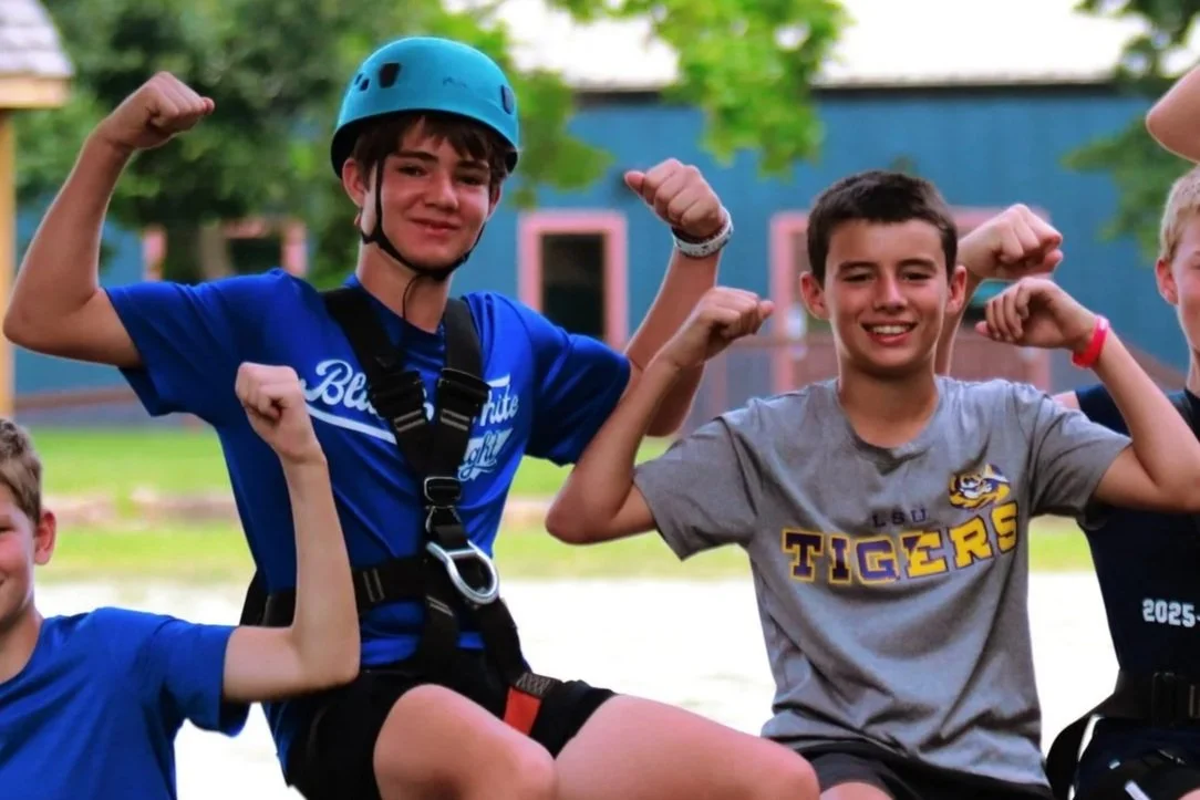 Two young men flexing their arms, smiling, and wearing helmets.