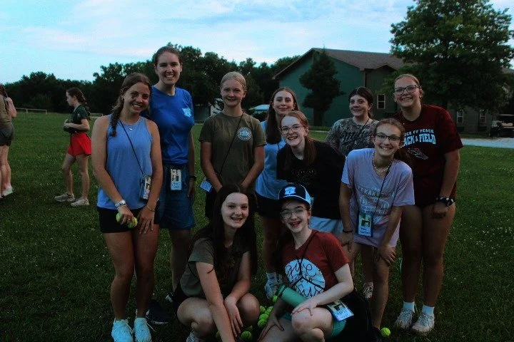 Group of girls in casual clothes and glasses, smiling outdoors on a grassy field during daytime.