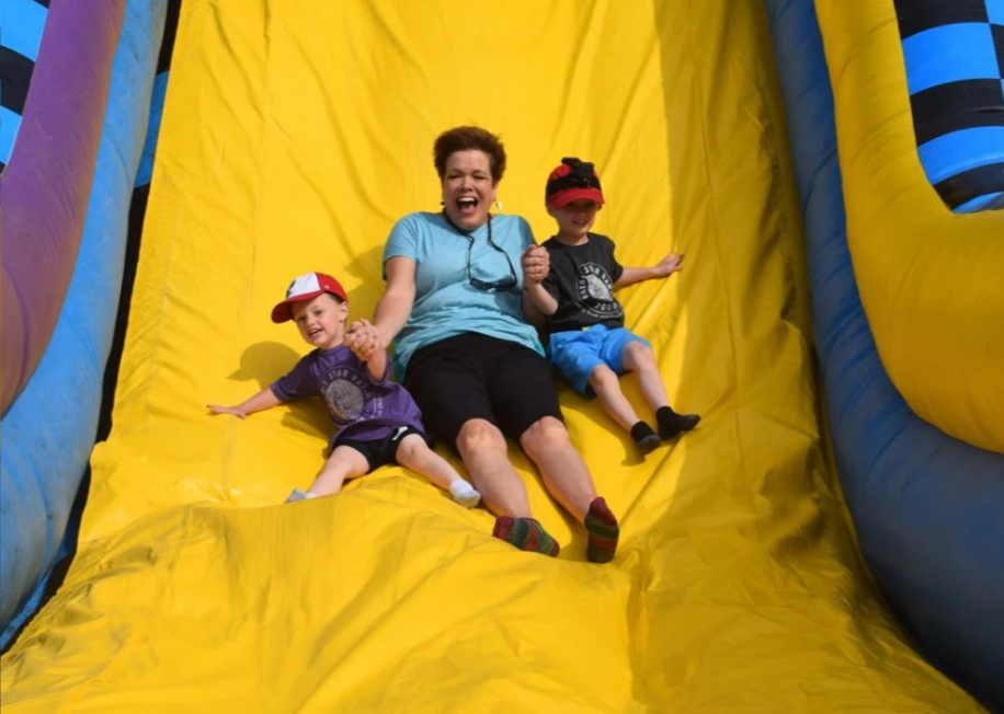 A woman and two children enjoying a slide in an inflatable bounce house.