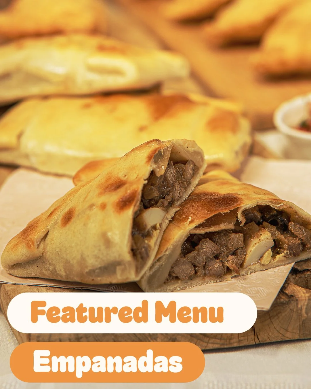 Close-up of an empanada with a crispy golden-brown crust, showing a meat and vegetable filling inside, placed on a wooden surface with additional empanadas and a small dish in the background. Text overlays reading 'Featured Menu' and 'Empanadas' in orange and white.