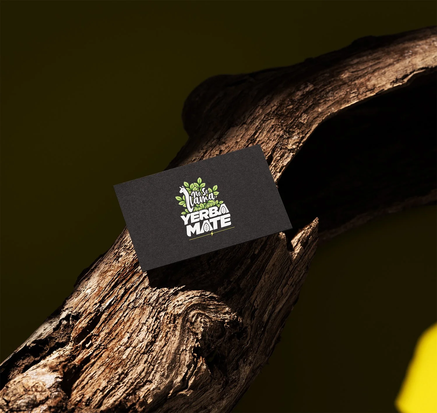 A black card with green and white text and graphics, placed on a large, textured tree branch. The card features a logo with a llama and leaves, and the words "No Se LaMina Yerba Mate."