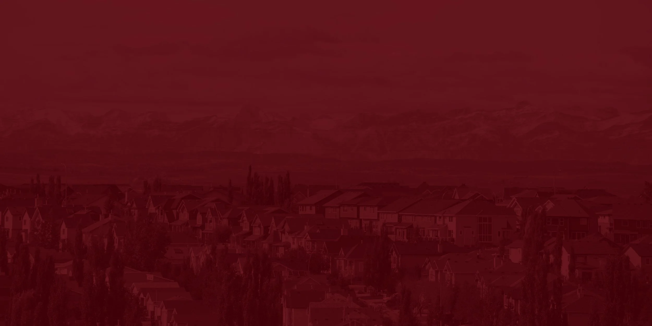 A cityscape with houses and trees under a red-tinted sky with clouds.