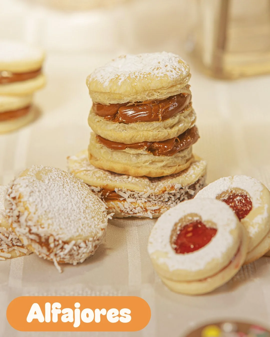 Assorted alfajores, including layered cookies with caramel filling, coconut-covered cookies with jam, and powdered sugar-covered cookies with jam notes, arranged on a table.