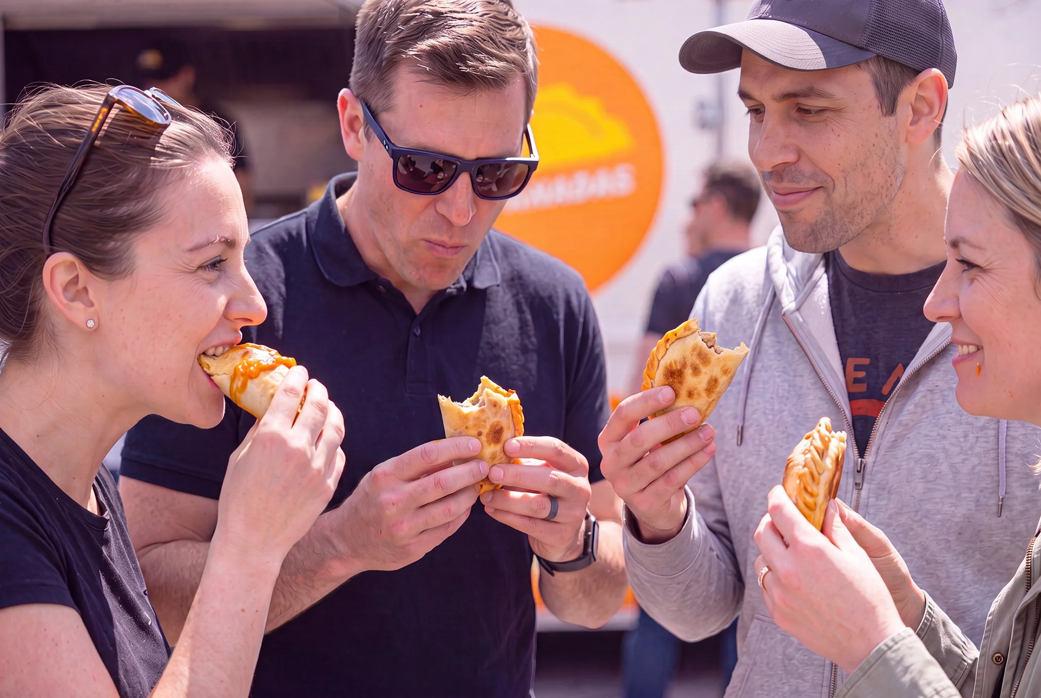 Group of people enjoying eating pizza outdoors on a sunny day.