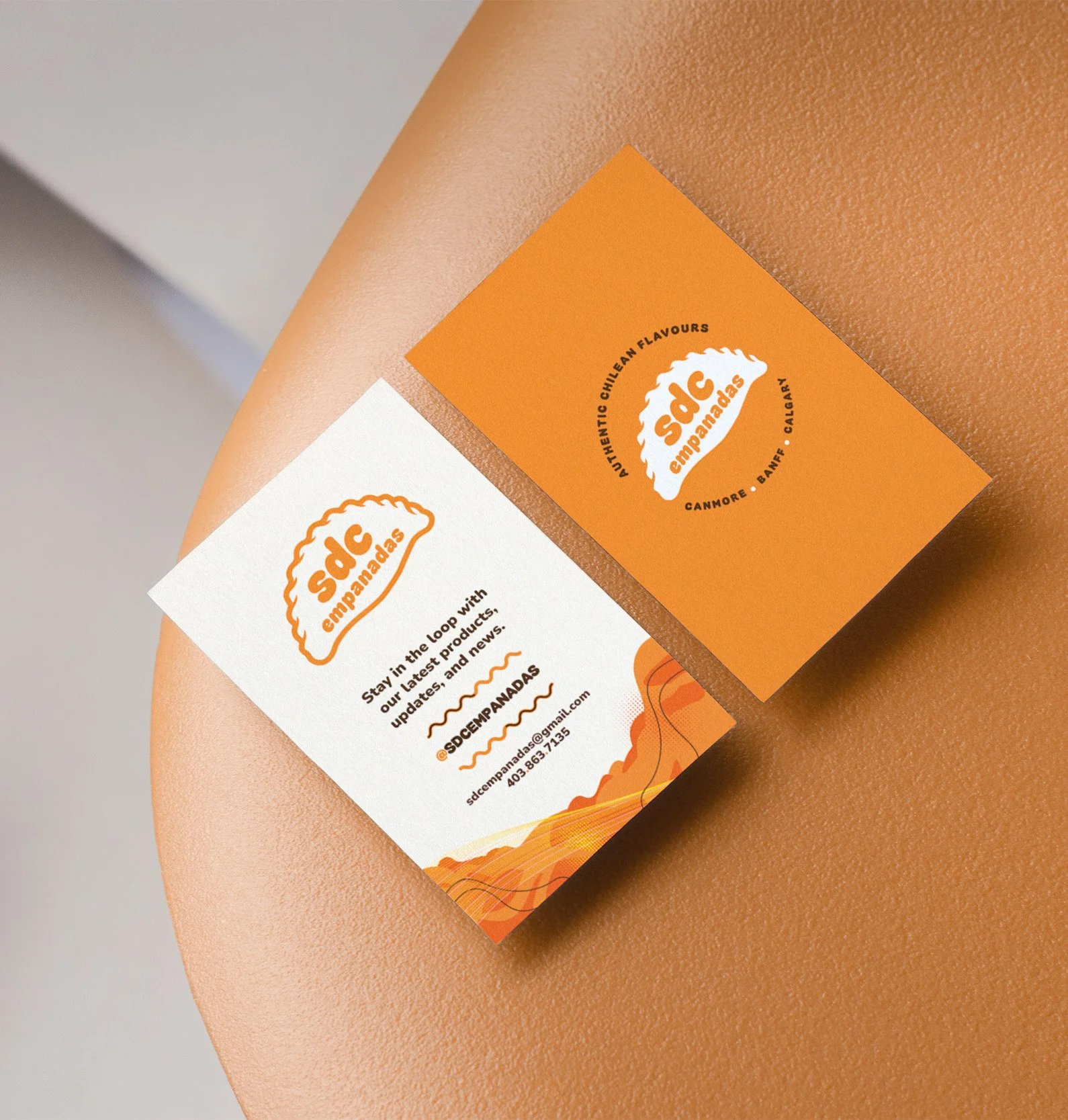 Close-up of two business cards for Sad Empanadas on a person's arm. The cards are orange and white with the company's logo and contact information.