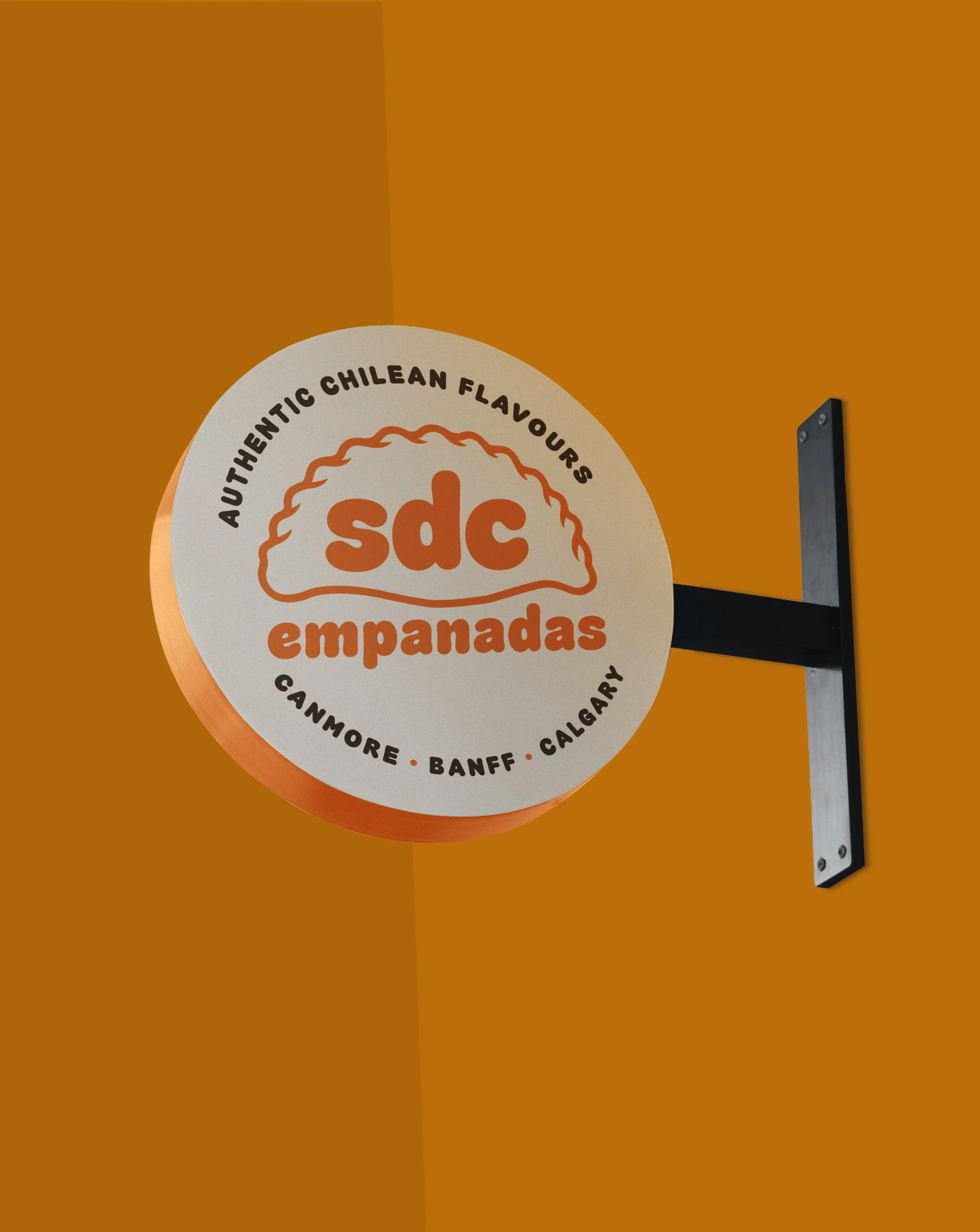 A round sign on a wall advertising empanadas with a logo and the words 'Authentic Chilean Flavours,' along with the locations 'Canmore, Banff, Calgary'.