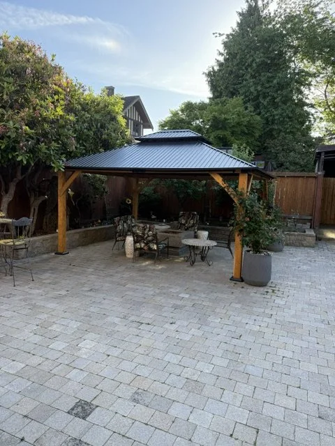 Outdoor patio area with a metal-roof gazebo, outdoor furniture, potted plants, and a wooden fence