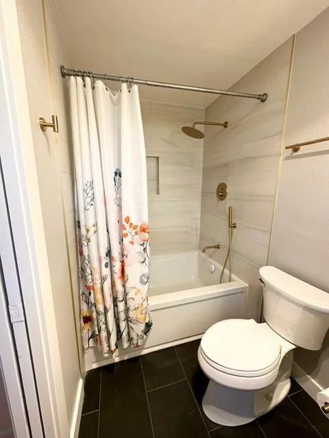 Bathroom with a bathtub and shower, white shower curtain with floral design, and a toilet in a small space.