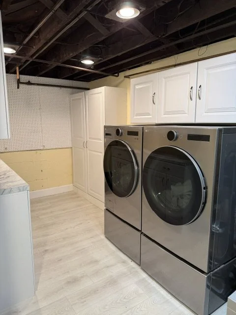Laundry room with a white cabinet, a yellow wall, a pegboard, and gray front-loading washing machine and dryer.