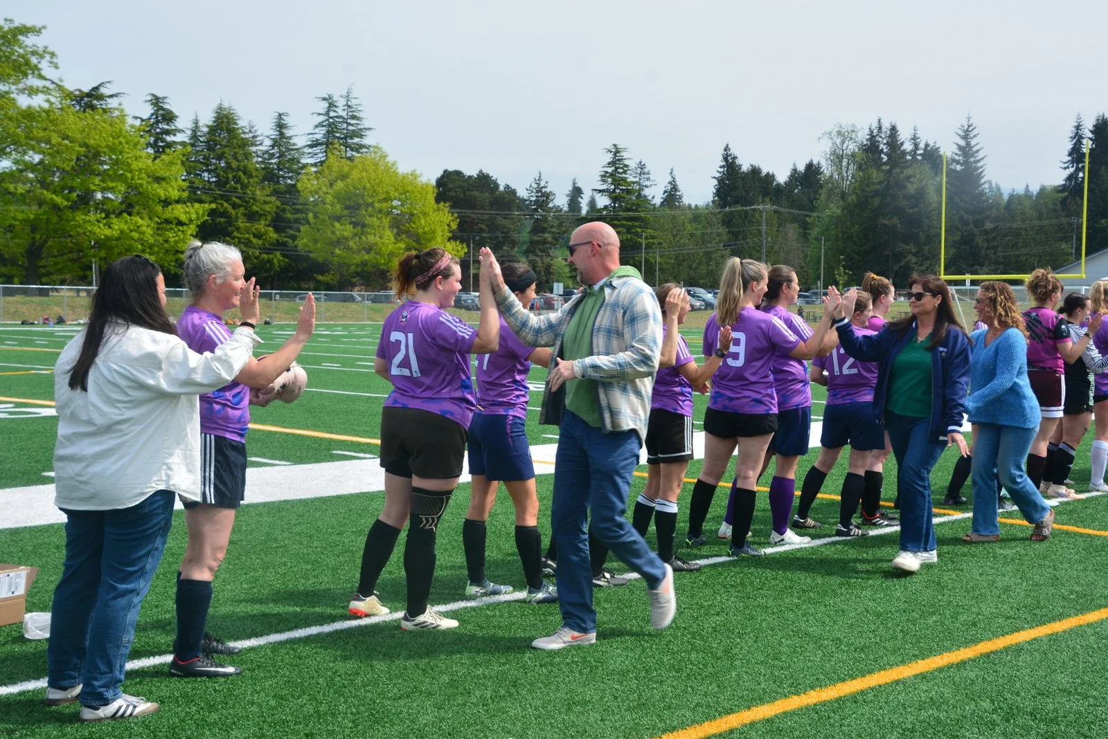 A women's soccer team on the field giving each other high-fives during or after a game, with some people clapping and celebrating.