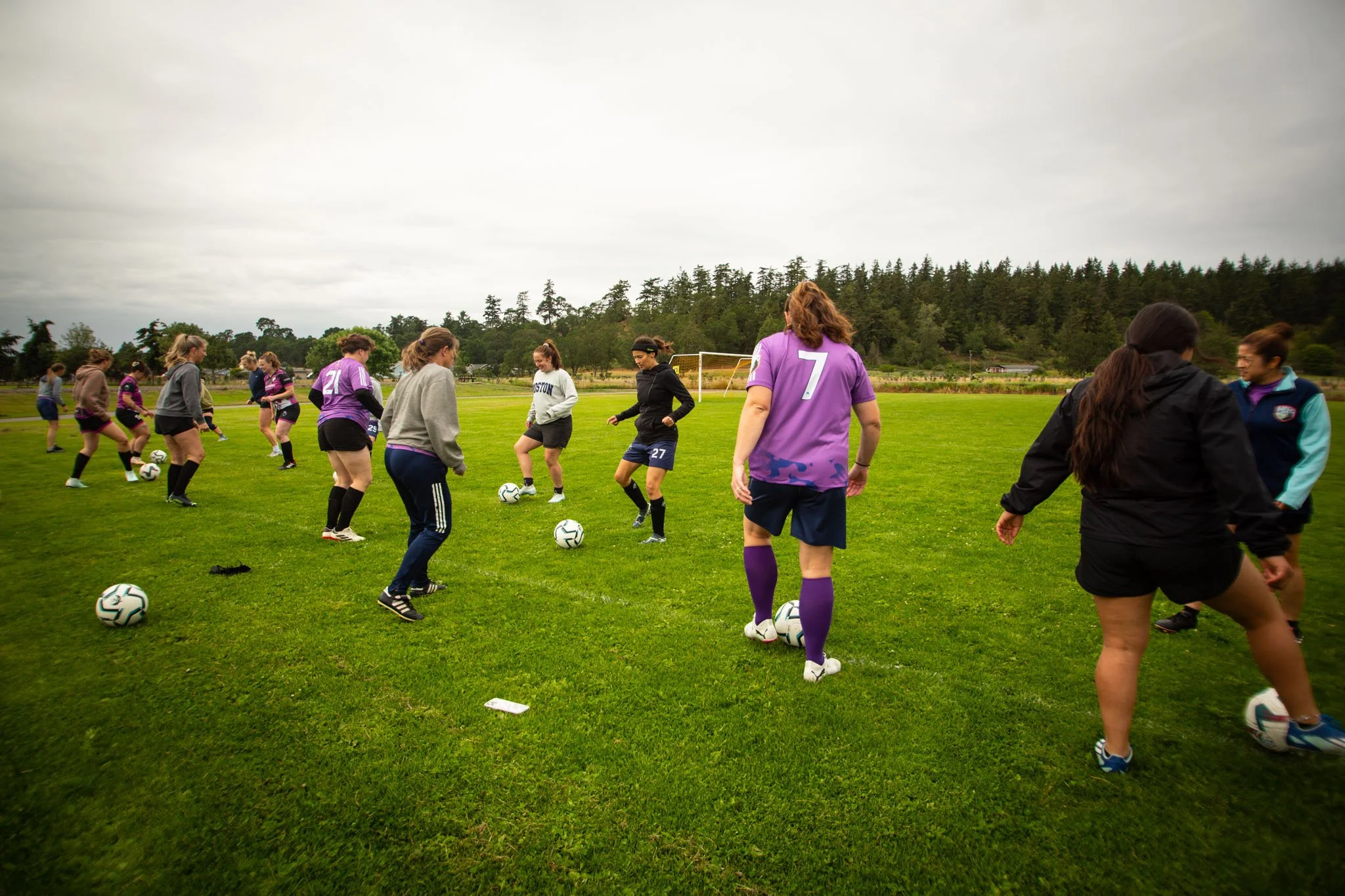 Women practicing soccer drills on a grassy field.