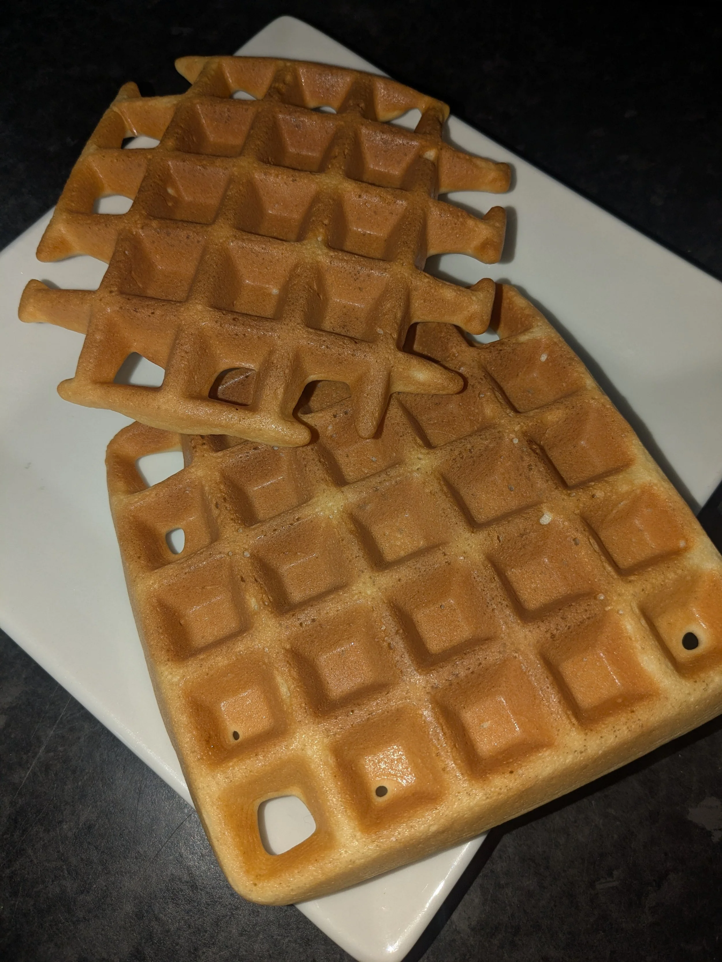 Close-up of three golden-brown waffles with deep square pockets on a white rectangular plate.