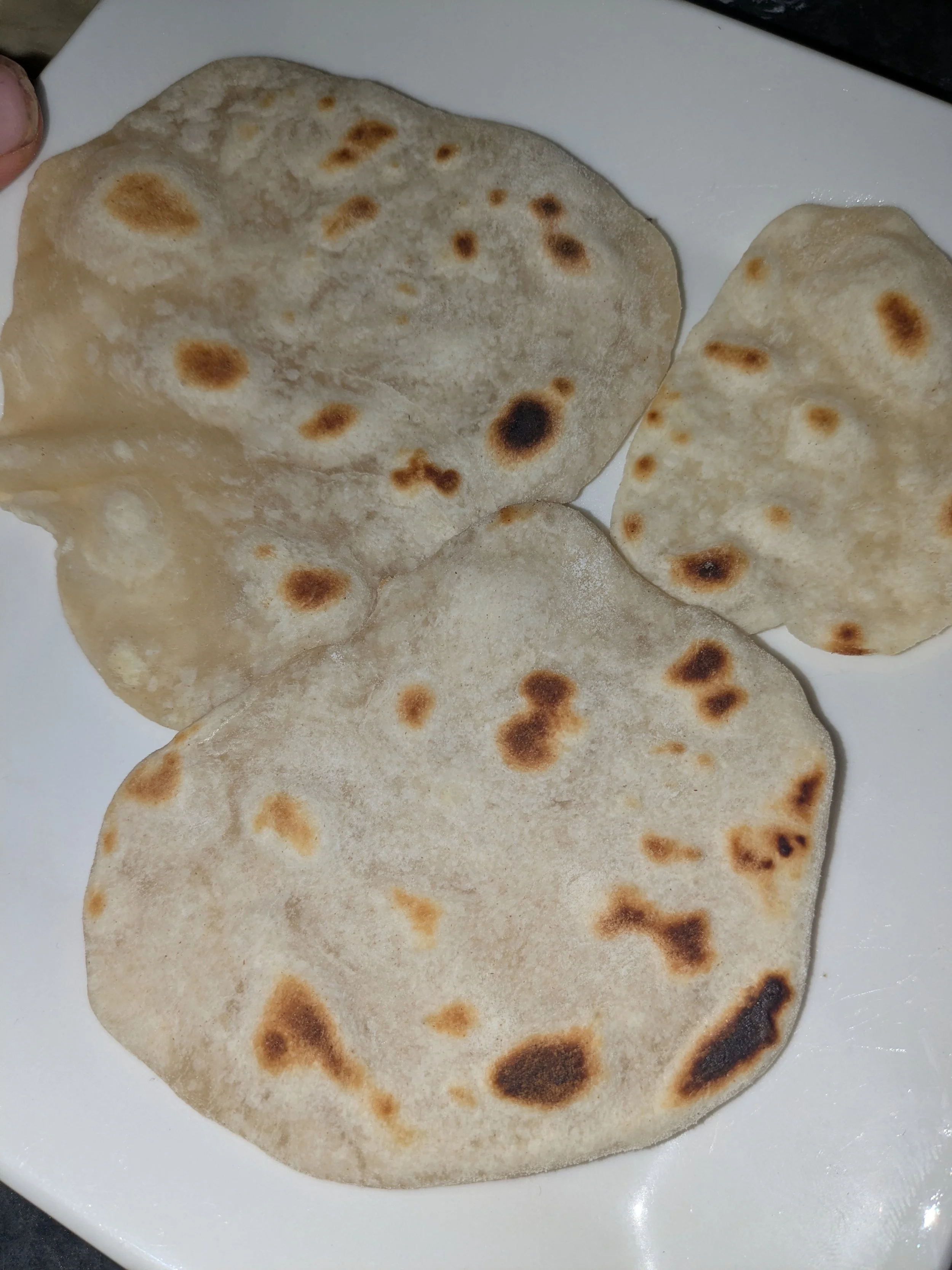 Close-up of three pieces of naan bread on a white dish, showing their round shape and browned spots from cooking.